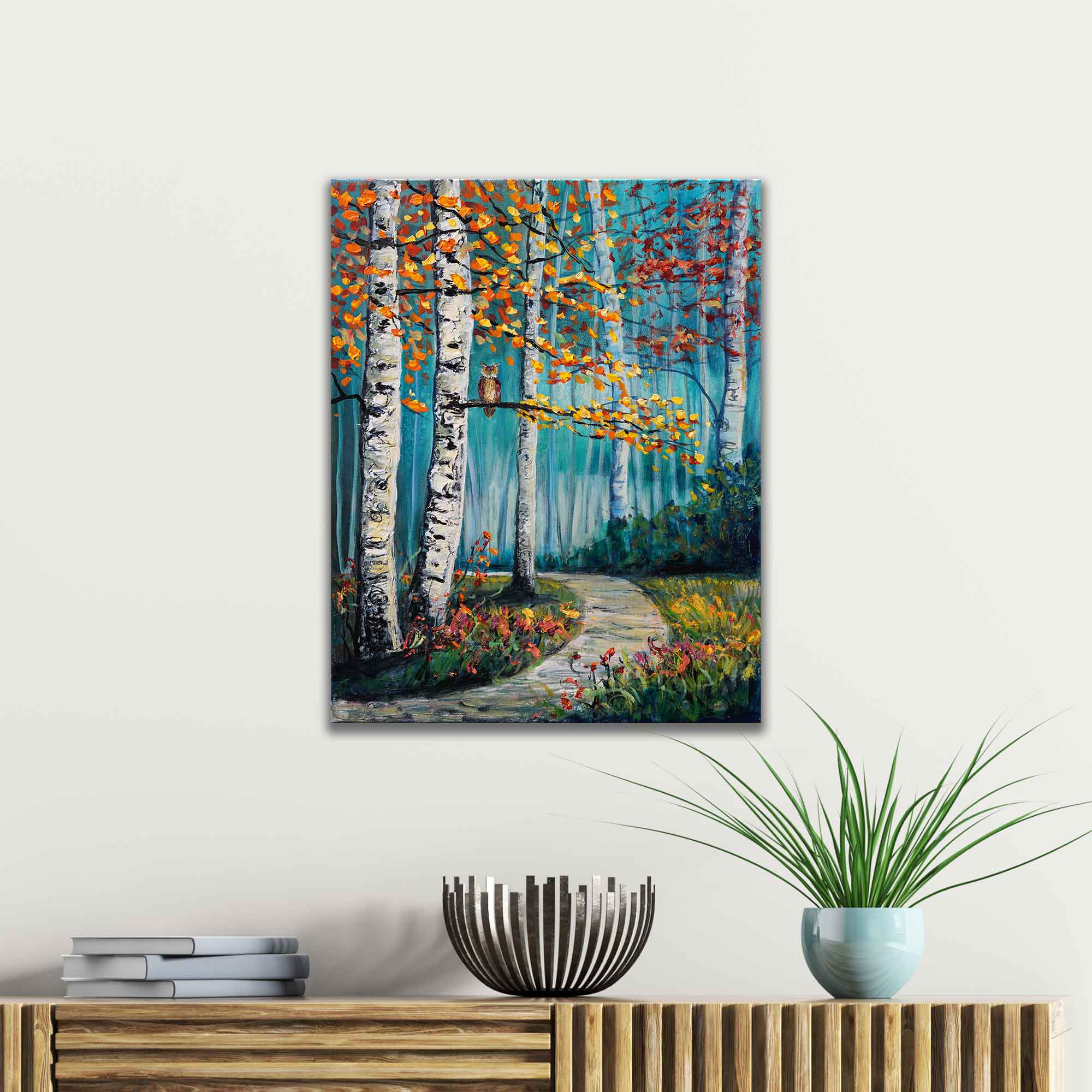 Painting of a forest scene with trees and flowers on a wall above a wooden console table.